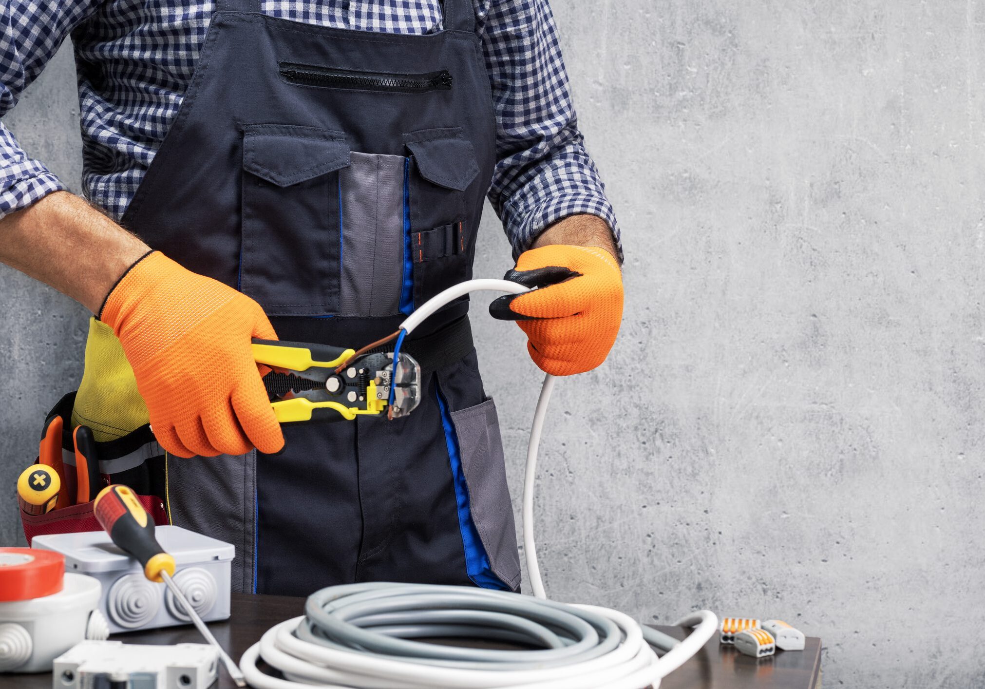 electrician worker striping the insulation of wires. electrician working against concrete wall.
